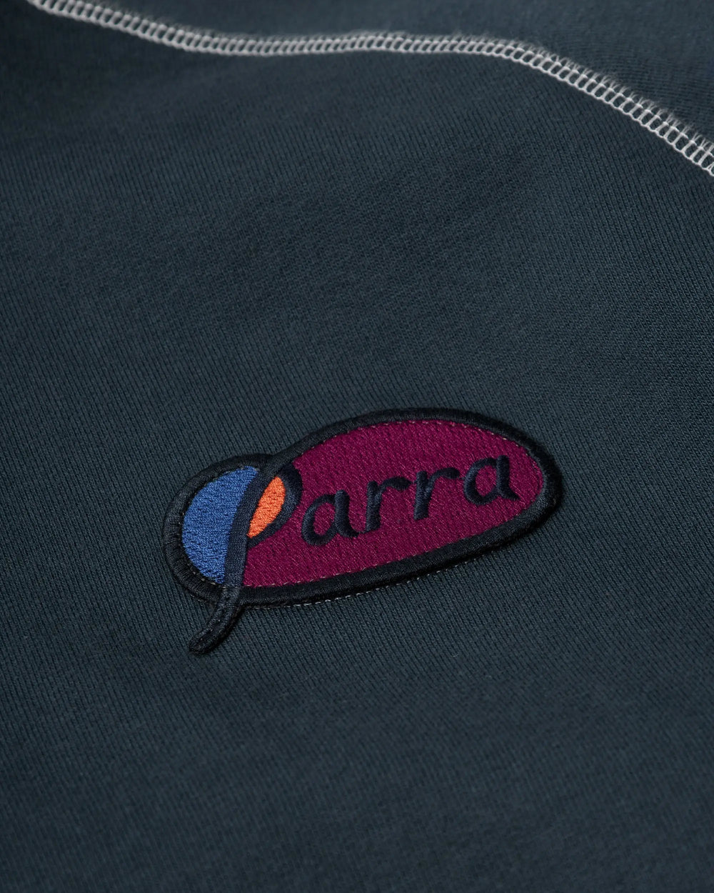 Embroidered Parra script logo patch detail on a dark blue hooded sweatshirt.
